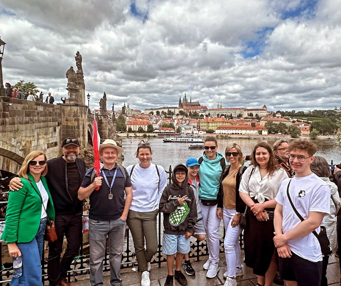 Jurek i uczestnicy wycieczki pod Mostem Karola z panoramą Pragi